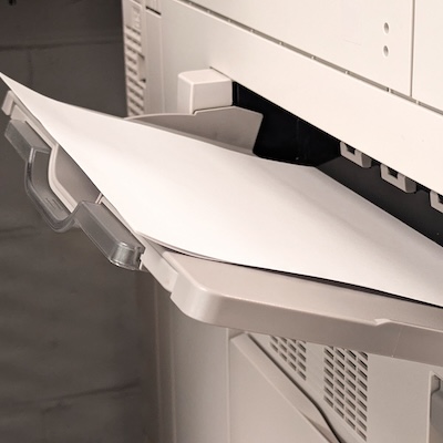 Open paper tray of a printer with white paper loaded and ready for printing.