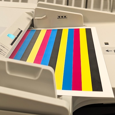 Printed test page with vertical stripes in black, cyan, magenta, and yellow emerging from a printer’s output tray.