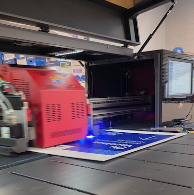 A close-up of a printing machine in action, featuring a red component and blue light as it prints on a sheet.