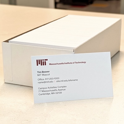 A business card using the MIT standard template rests next to a box full of business cards.